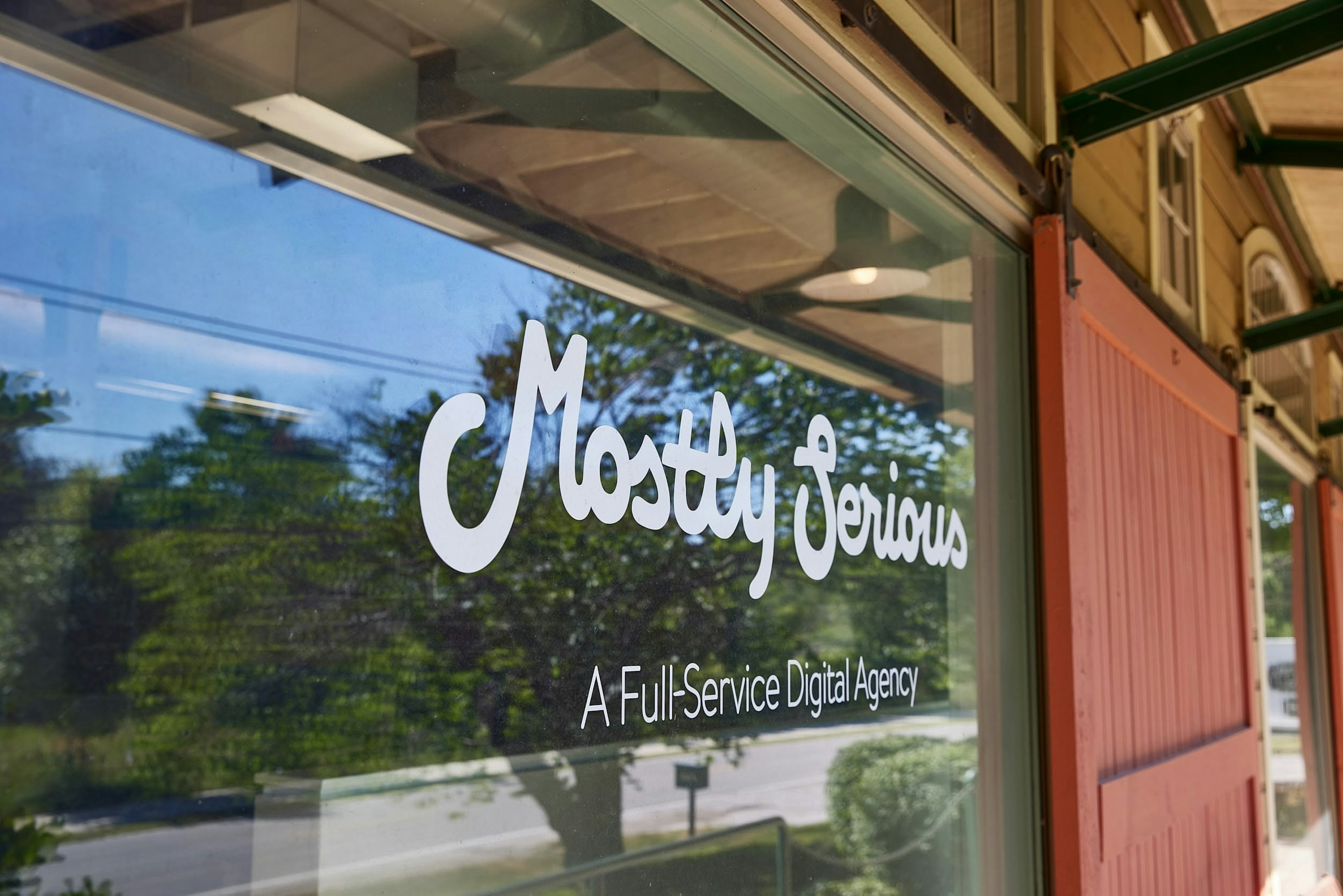 Mostly Serious office window with the company logo and the words “A Full-Service Digital Agency” reflected against trees and the street outside.