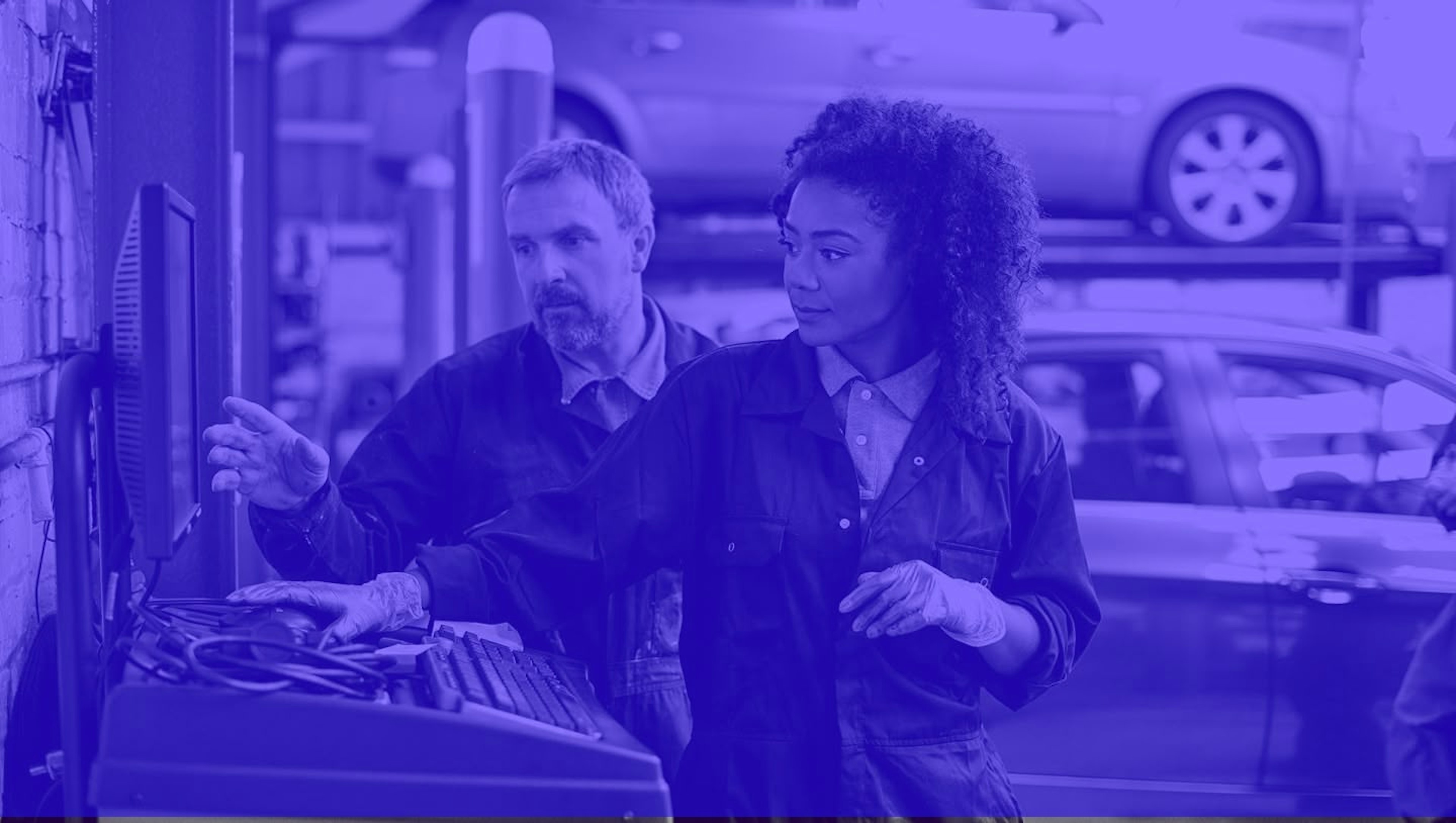 Two automotive technicians collaborating in a modern auto shop, with a purple duotone treatment. A senior technician points at diagnostic equipment while training a young woman with curly hair, representing the career mentorship opportunities in the automotive tech industry.