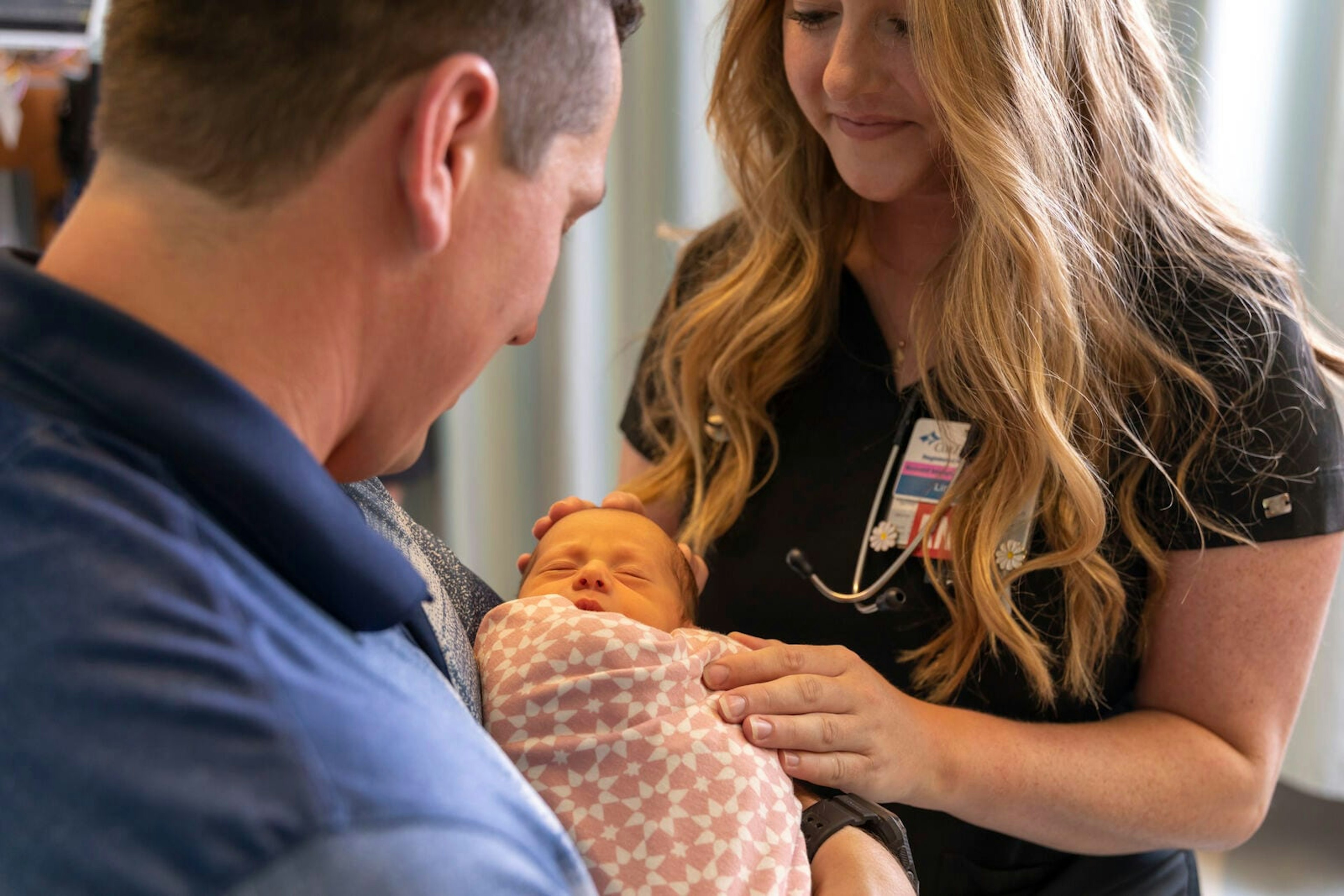 A nurse holding a newborn while speaking with a parent.