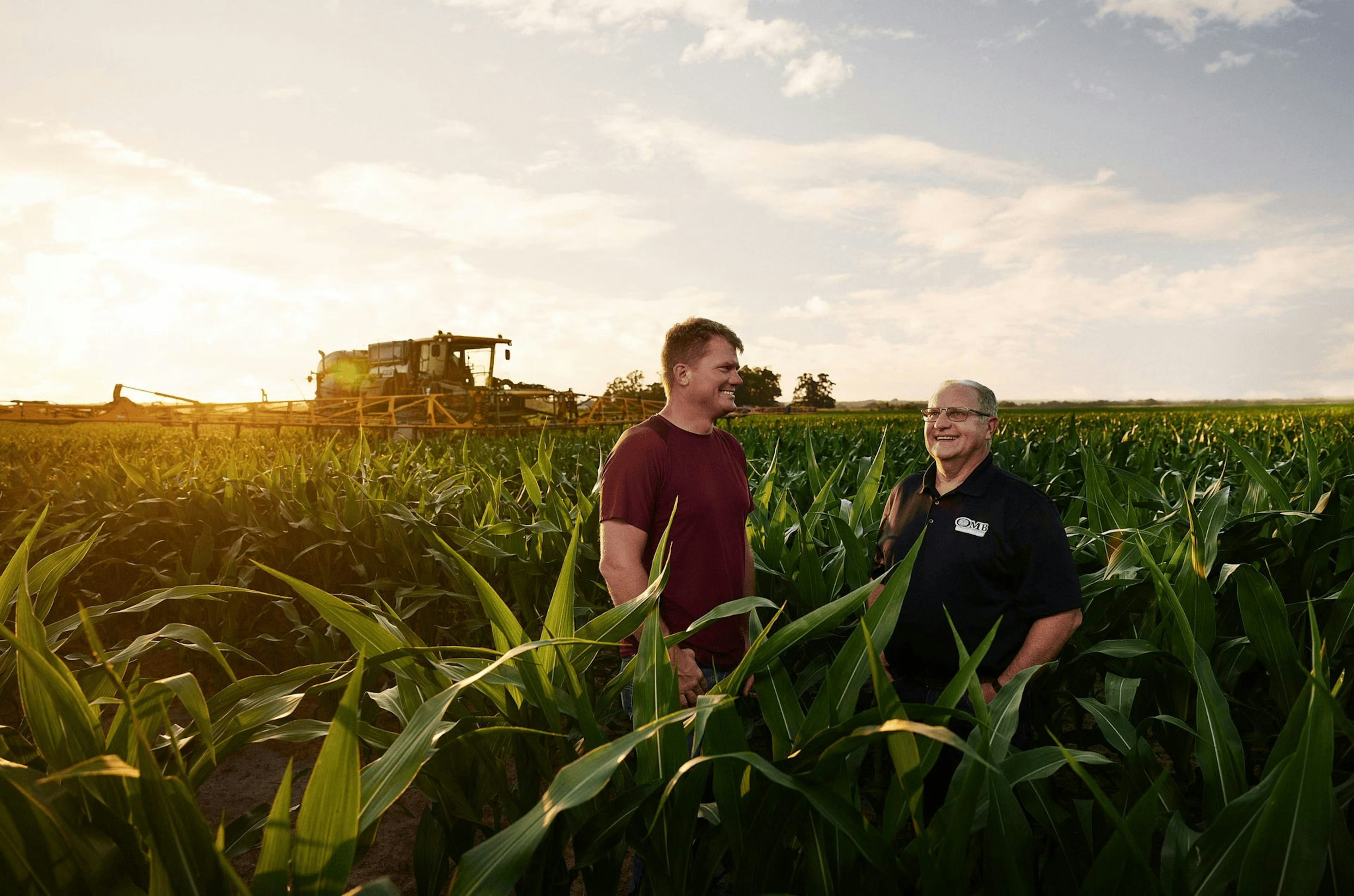 Two people standing in a corn field at sunset.