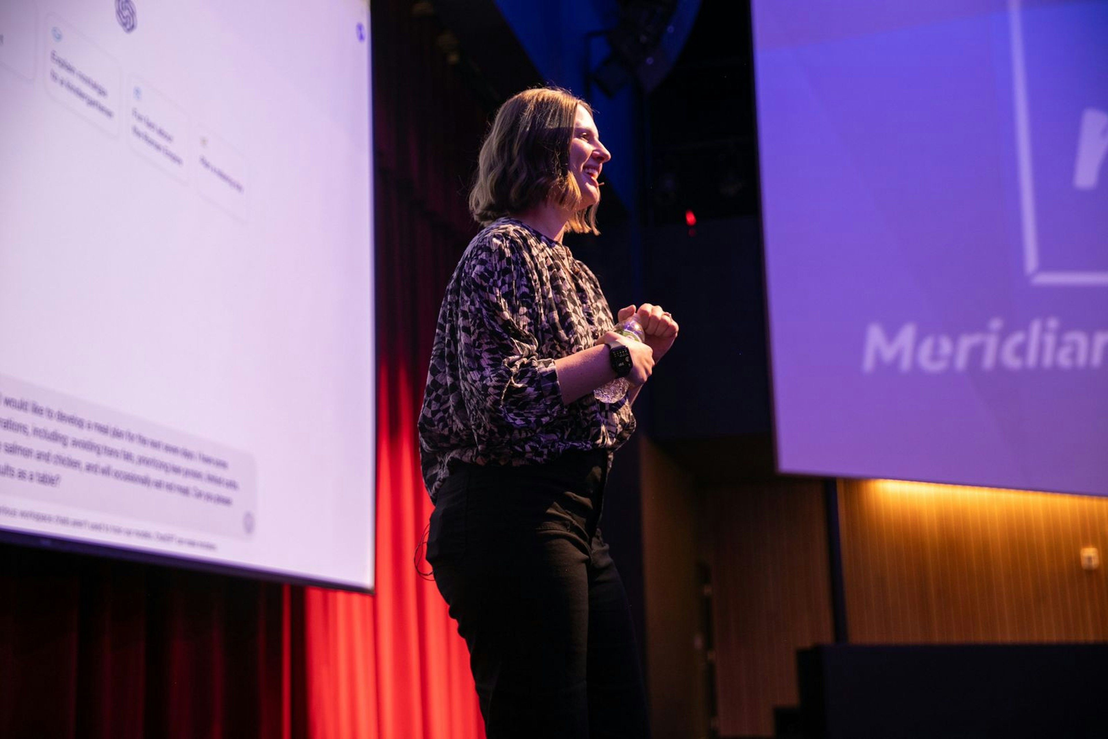 Facilitator speaking on stage in front of a large projected AI interface.