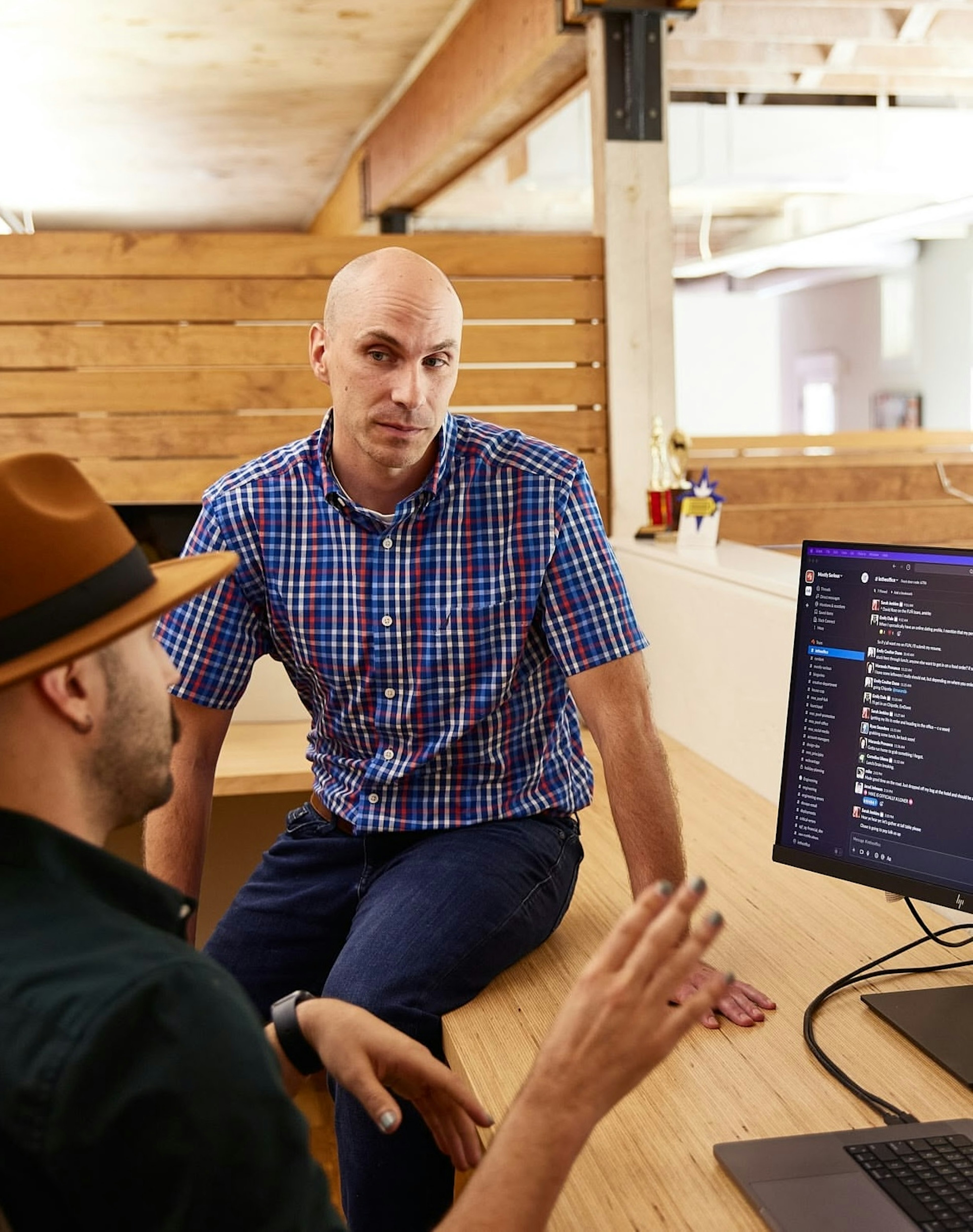 Two teammates in discussion at a desk with a laptop and messaging app on screen.
