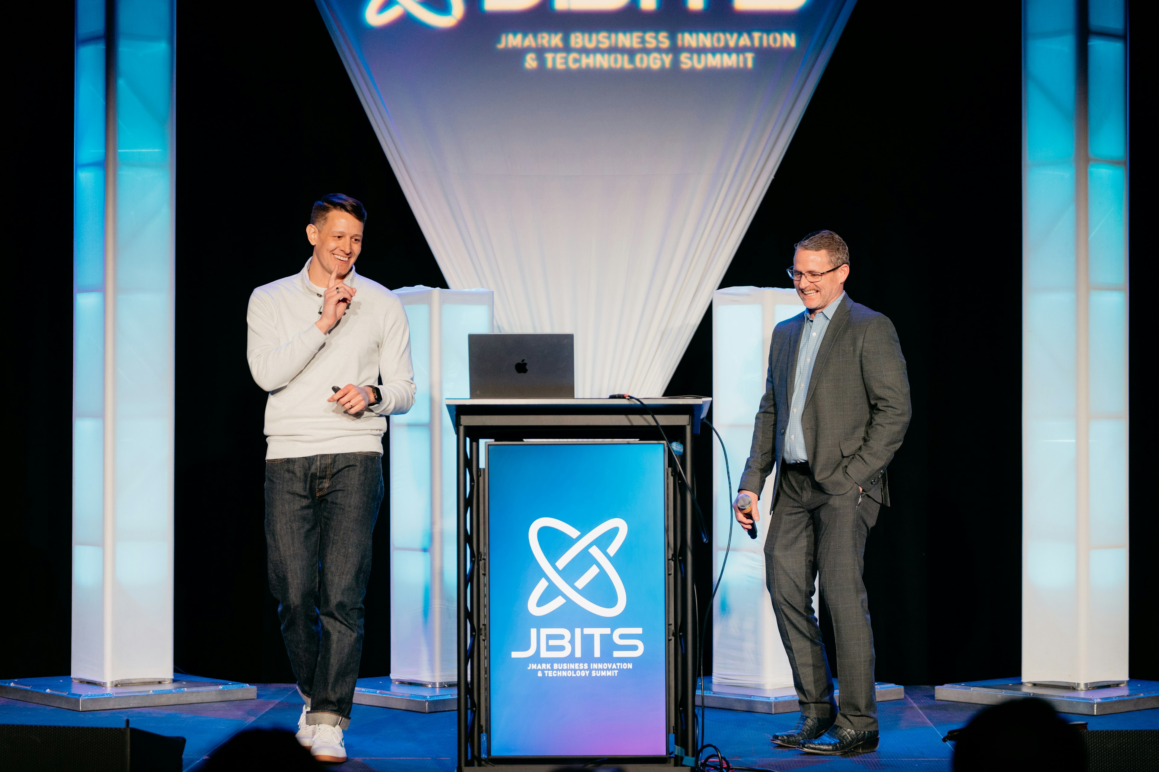 Two speakers presenting on stage at the JMARK Business Innovation & Technology Summit.